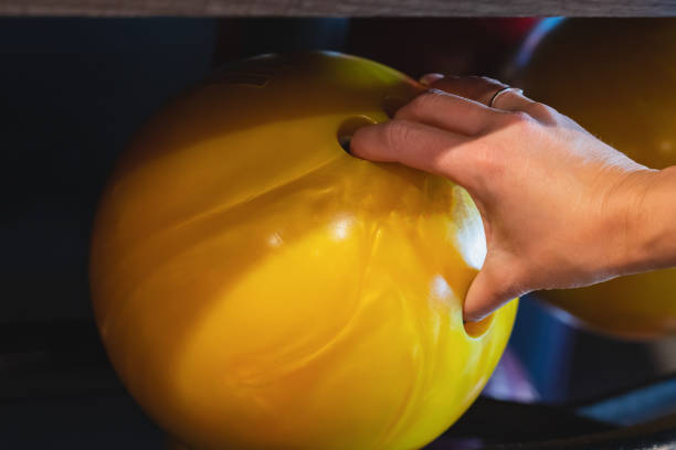 A woman's hand takes a yellow bowling ball, close-up photo.