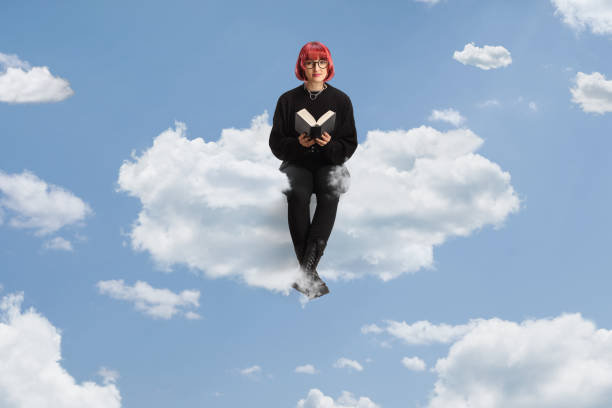 istock Young woman with red hair sitting on a cloud and reading a book 2149784096