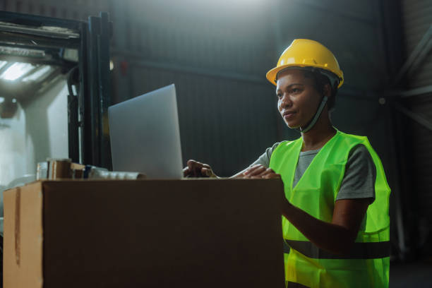 istock Female customs warehouse worker wearing a hardhat working on a laptop 2149784472