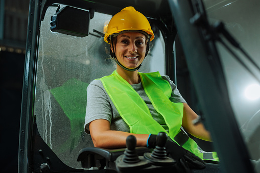 Female warehouse worker sitting and smiling in a forklift while on duty in a warehouse