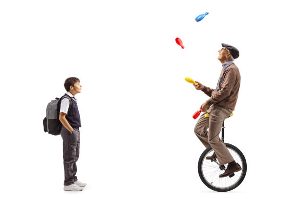 istock Boy standing and watching an elderly man riding a mono cycle and juggling 2149784813