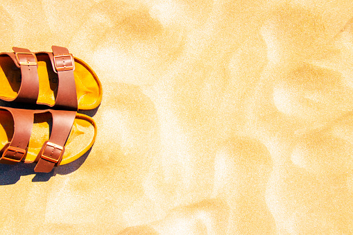 Summer vacation background. Brown shoes or sandals on a golden sunny sandy beach. Advertisment travel.Copy space. Top view.