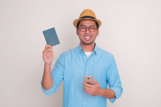 istock A man smiling at the camera while holding mobile phone and passport document 2149786080