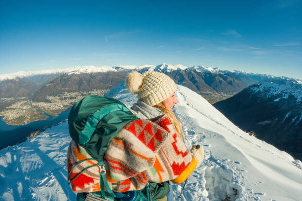Close up of female adventurer on a steep snowy hill. She's focused on moving through the untouched snow, with mountains and a sunny sky in the distance. She's dressed in winter gear and carrying a backpack with a smile on her face.