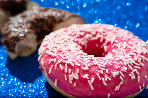 Close-up of tasty pink and chocolate doughnut against shiny blue background