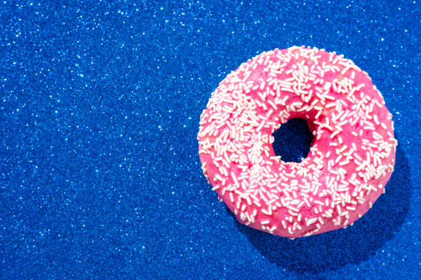 High angle view of a pink donut with crumbs on a sparkling blue background