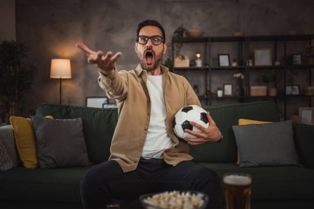 istock A handsome young man is watching a soccer game on TV at home 2149790915