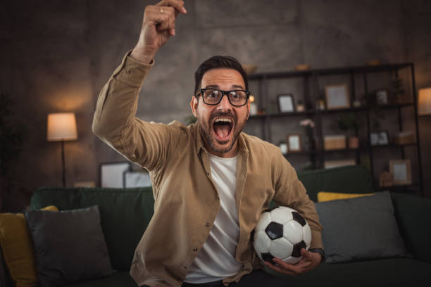 istock A handsome young man is watching a soccer game on TV at home 2149790917