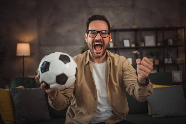 istock A handsome young man is watching a soccer game on TV at home 2149790938