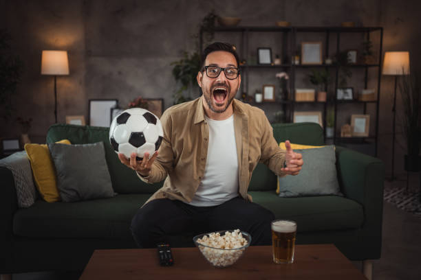 istock A handsome young man is watching a soccer game on TV at home 2149790955