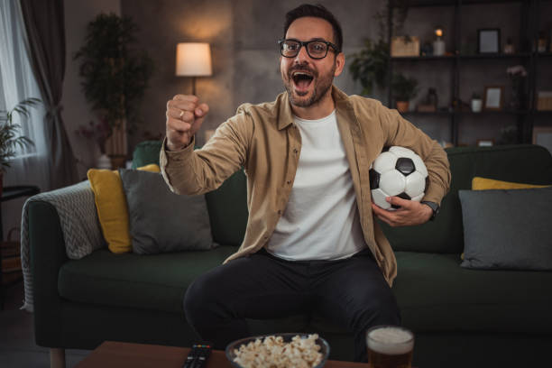 istock A handsome young man is watching a soccer game on TV at home 2149790957