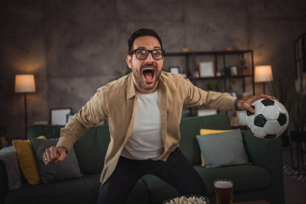 istock A handsome young man is watching a soccer game on TV at home 2149791022