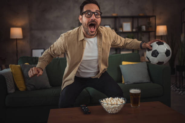 istock A handsome young man is watching a soccer game on TV at home 2149791027