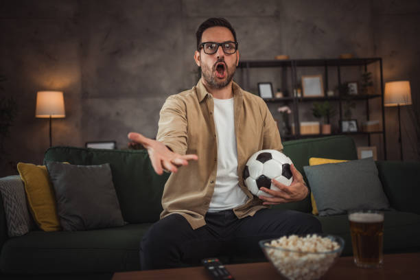 istock A handsome young man is watching a soccer game on TV at home 2149791030