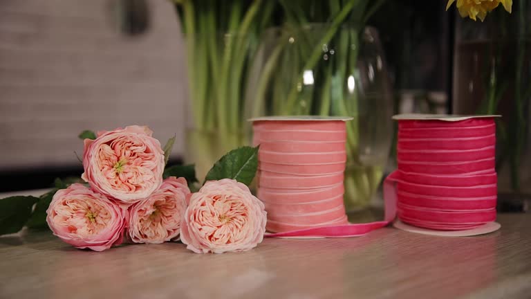 Flower shop concept. Ribbon for bunch of roses lying on the table, pink peony flowers close up