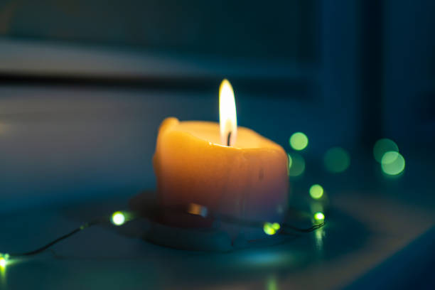 Burning candle with a small garland standing on a windowsill late in the evening night.poor christmas holiday.