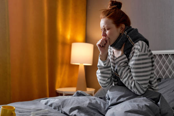 unhealthy week red-haired woman in scarf and sweater coughing, closing mouth with fist unhealthy week red-haired woman in scarf and sweater coughing, closing her mouth with fist, closeup side view portrait night hospital bed stock pictures, royalty-free photos & images