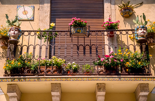 A small balcony decorated with colorful ornamental flowers and a wrought-iron balustrade in Mediterranean style in the sunshine with the balcony door closed