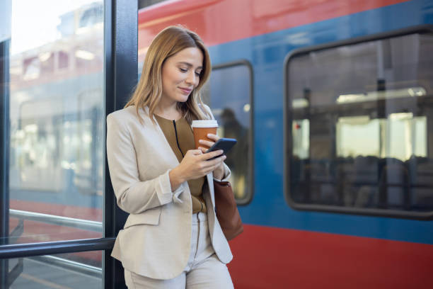 istock A beautiful woman is using a mobile phone at a train station while waiting to get into a train car 2149794137