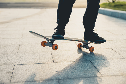 A close-up shot focuses on an Asian skateboarding enthusiast using his skateboard to go to a place he wants to visit, and practicing his skateboarding skills along the way. The camera is zoomed in on his feet and the skateboard.