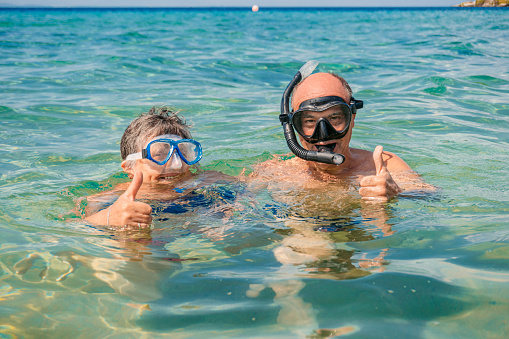 Portrait of a senior couple giving thumbs up while snorkeling in the sea in Sithonia in Greece.