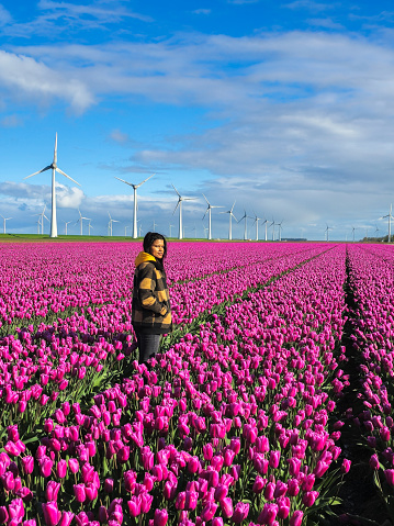 An Asian woman is standing proudly in a field of vibrant purple flowers, surrounded by the beauty of nature in full bloom on a sunny day. Asian women with windmill turbines in the background