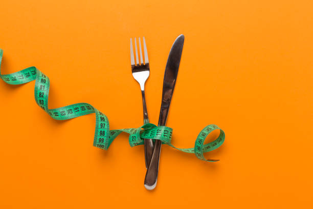 Knife and fork wrapped in tape measure on color background, top view