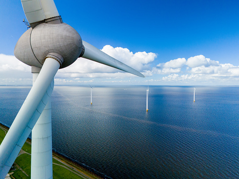 A wind turbine stands tall in the ocean, its blades spinning in the spring breeze, harnessing the power of the wind to generate clean energy. windmill turbines in the Noordoostpolder Netherlands