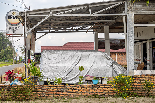 Samosir Island, Lake Toba, North Sumatra, Indonesia - February 1st 2024:  Minibus under a tarpaulin outside a residential building