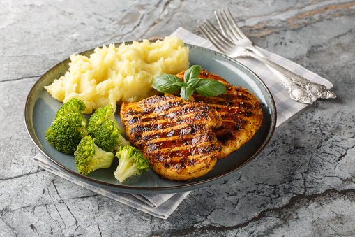 portion of grilled chicken breast with a side dish of mashed potatoes and broccoli close-up in a plate on the table. Horizontal