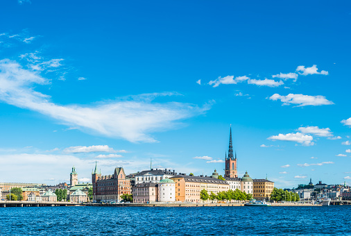 Panoramic view over the blue waters of Riddarfjarden to the historic waterfront of Gamla Stan and Sodermalm beneath the blue skies and white fluffy clouds of a sunny summer afternoon in the heart of Stockholm, Sweden's vibrant capital city.