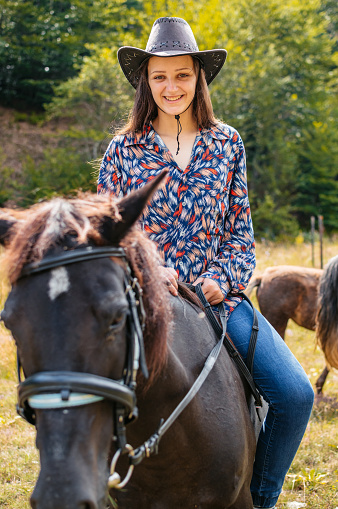 Portrait of a young cowgirl riding a horse on the farm.