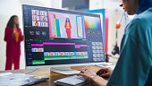 In A Vibrant Film Studio, A Young Caucasian Female Editor Fine-tunes A Colorful Video Project On Her Monitor, Showcasing A Woman In A Red Suit, Enhancing Storytelling In Modern Videography.