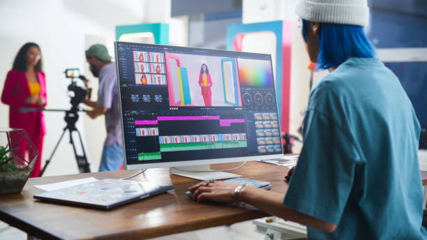 young caucasian female editor with blue hair works on video editing software, while a hispanic male videographer records a black female host in a vibrant studio setting, enhancing media production. - videoproductie fotos stockfoto's en -beelden