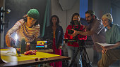 Young Diverse Team Of Cinematographers Engaged In A Lively Video Production Session On A Film Set, Focusing On A Creative Advertising Shoot With Vibrant Lighting And Dynamic Camera Work.