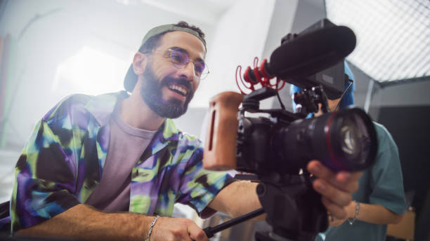 istock Young Male Cinematographer With Beard And Glasses, Smiling While Operating A Professional Camera In A Studio Setting, Capturing Footage For A Creative Advertising Project. 2149806664