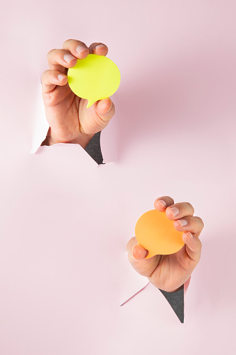 Human hand holding yellow and orange speech bubbles on pink background