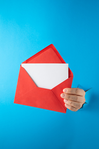 Hands break through paper with red envelope on blue background