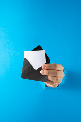 Hands break through paper with black envelope on blue background