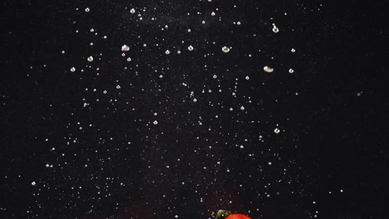 Group of fresh tomatoes falling into water with splash and bubbles isolated over black background