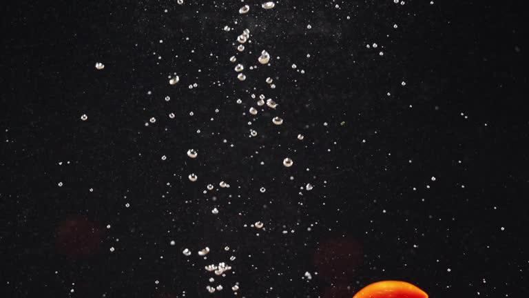 Red organic tomatoes dropping into the water with air bubbles against black background