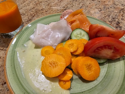 A green plate filled with assorted sliced vegetables sits next to a glass of refreshing orange juice