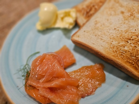 A blue plate is seen topped with slices of toast and smoked salmon