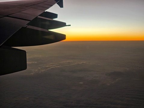 The wing of an airplane is silhouetted against the setting sun