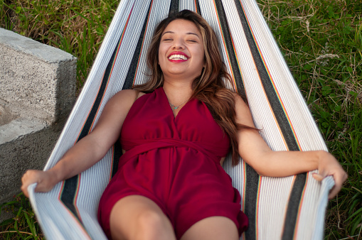 A cheerful tourist woman in a red dress resting in a hammock, laughter lighting up her face.