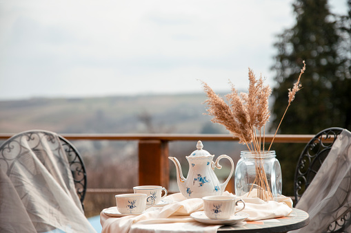 Shabby chic breakfast on balcony . Teapot and cups on a table. Outdoor breakfast on vacation