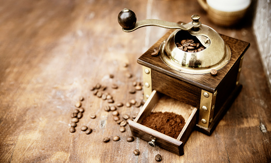 Roasted coffee beans and milled coffee in small wooden manual grinder with a brass handle.