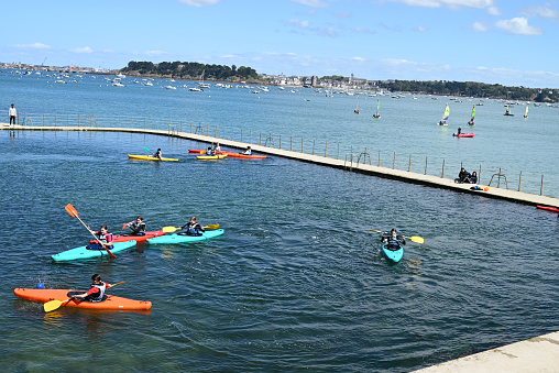 Dinard, France, april 18, 2024 : Kayakers in the seawater pool of the Priory of Dinard with the town of Saint-Servan in the background