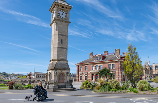 Barnstaple, UK. 18 April 2024. Wheelchair user with a dog at the Barnstaple Clock Tower and Museum in the town centre.