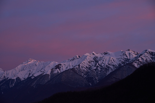 Snow-capped mountains bask in twilight's pink glow.